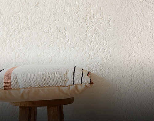 Stack of pillows in motion adding one at a time onto a stool in front of a white wall
