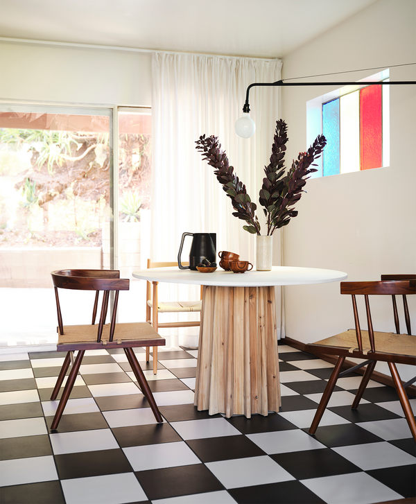 Round white top dining table with a wooden base on a black and white checker board floor