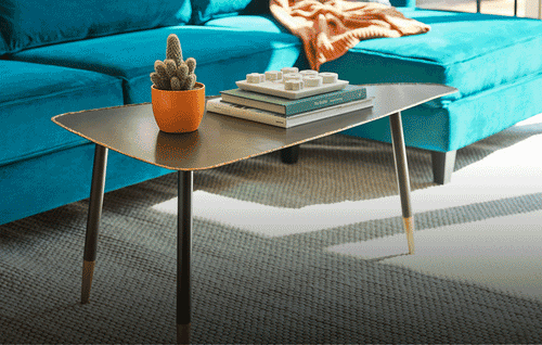 Blue sectional sofa on a grey rug with two brown triangular nesting tables in front in motion